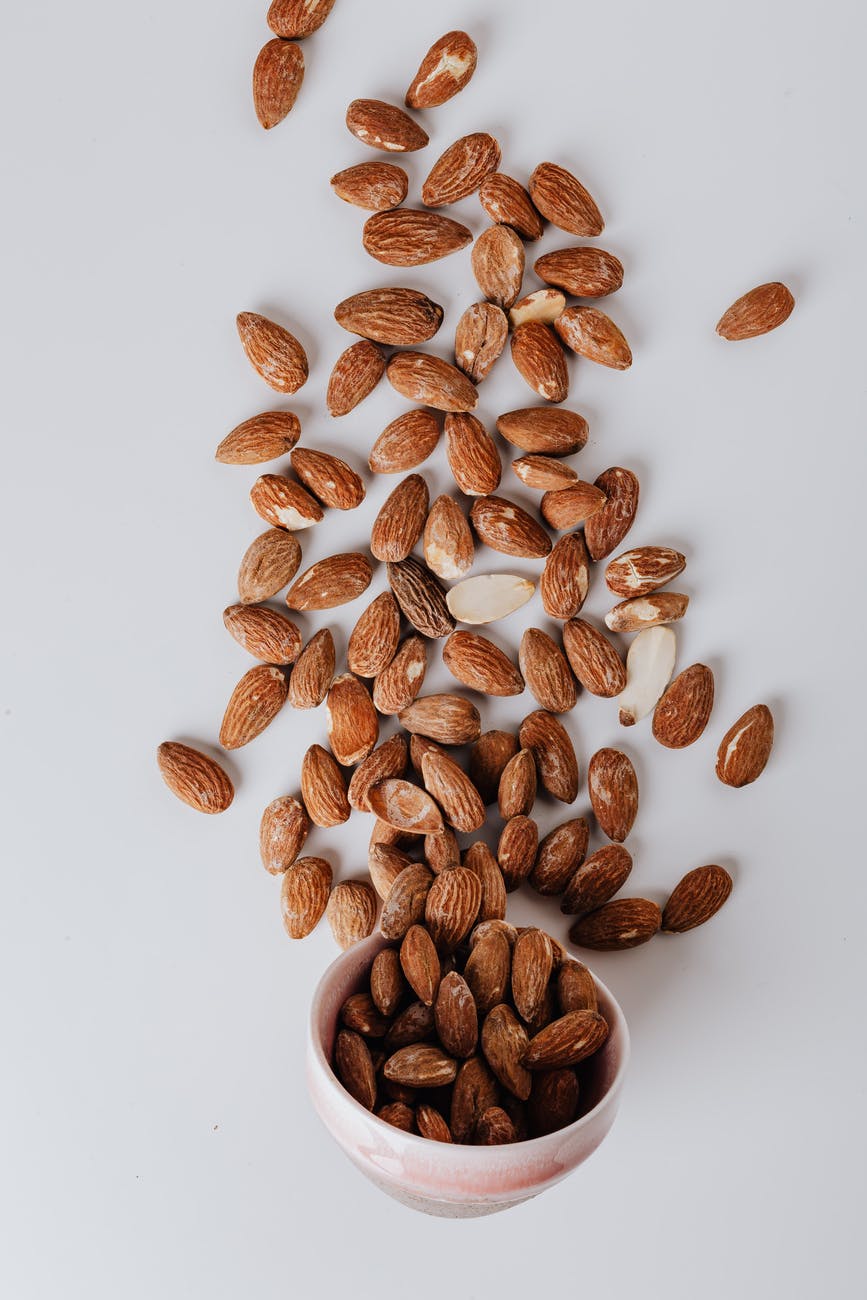 raw almonds spilled out of small ceramic bowl on table