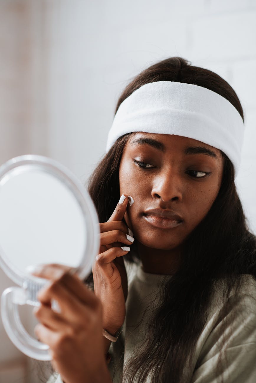 african american woman with mirror applying nourishing cream on face